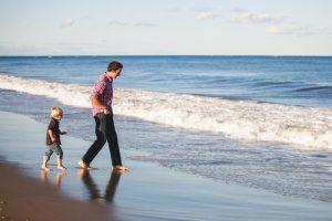 Man walks with child at beach. Men and relationships with their children can be beautiful and complex.